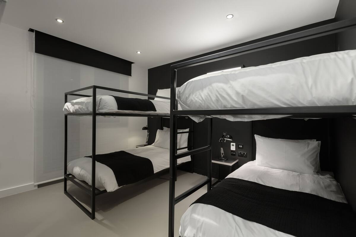 A modern hotel room with bunk beds, a bedside table with a lamp, and a wall-mounted TV.