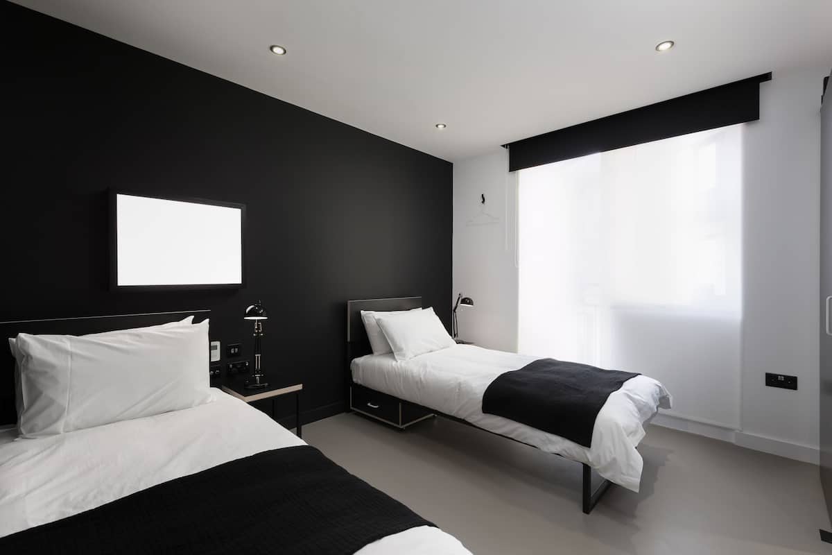 A modern hotel room with two beds, a large window, and a wall-mounted TV.