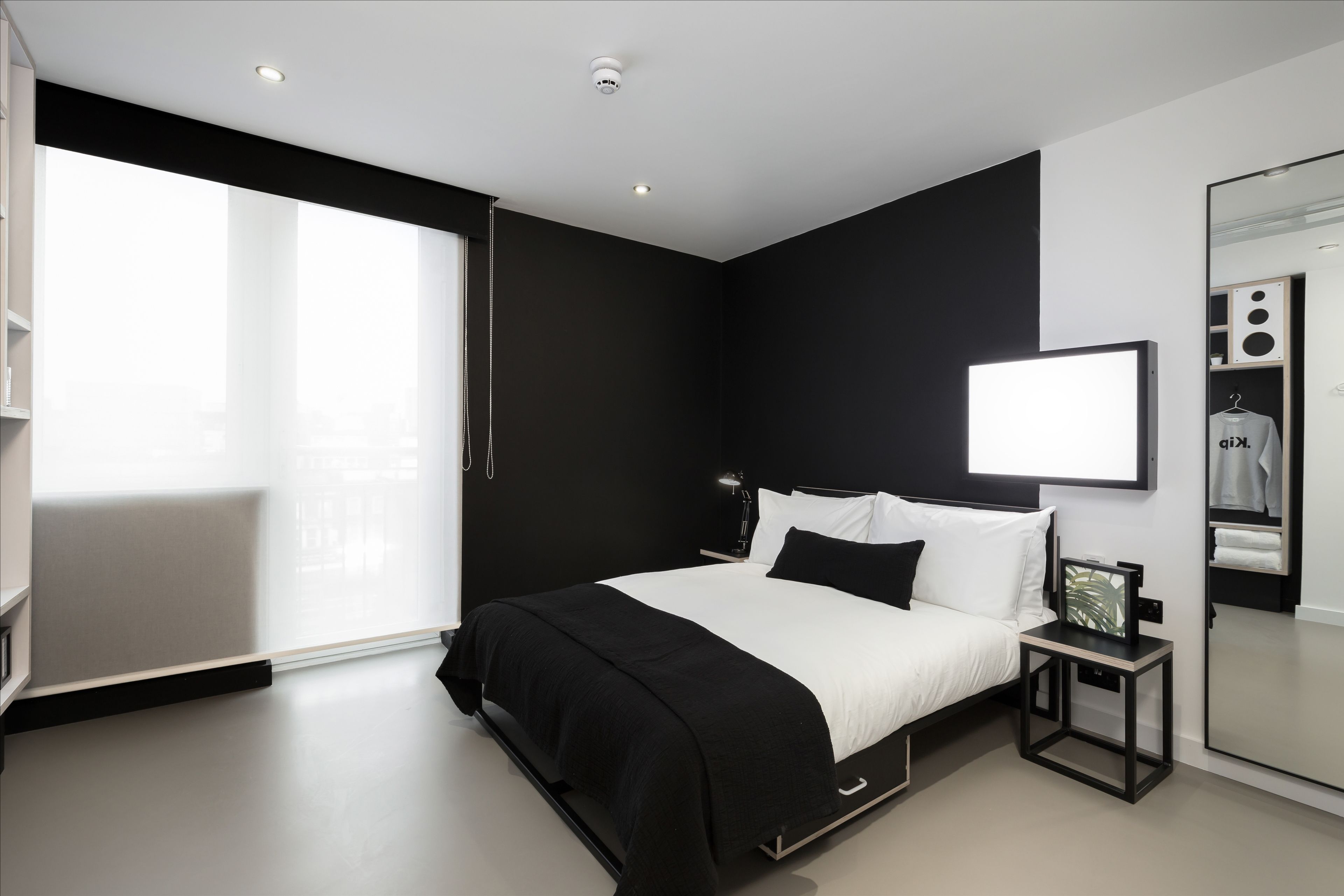 A modern bedroom with a large bed, a bedside table, a mirror, and a window.