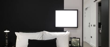 A modern hotel room with a large bed, a bedside table with a lamp, a framed picture, and a wardrobe.