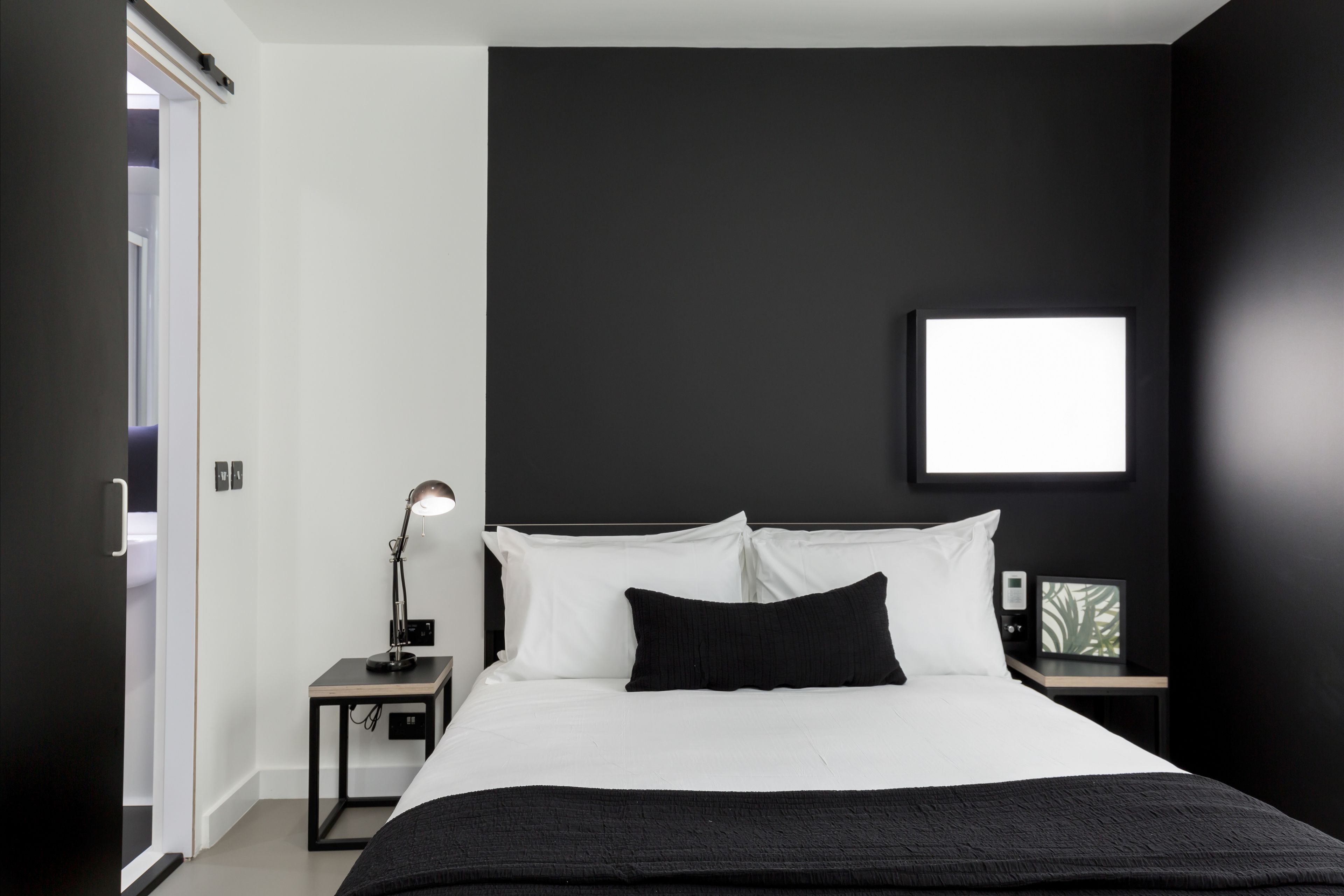 Ein modernes Schlafzimmer mit einem großen Bett, einem Nachttisch mit Lampe und einem gerahmten Bild an der Wand.