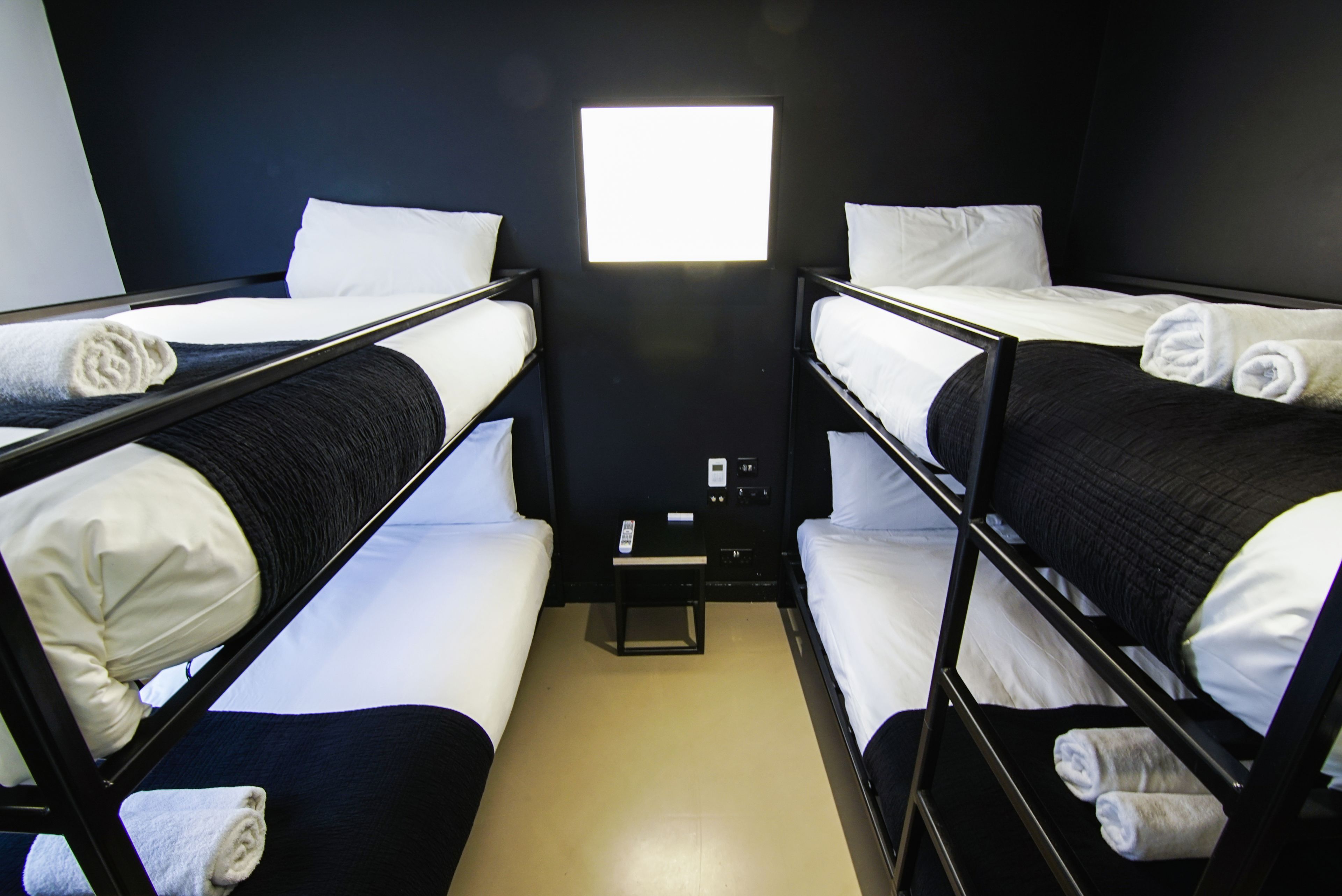 Una habitación con literas, ropa de cama blanca y una mesita de noche con lámpara.