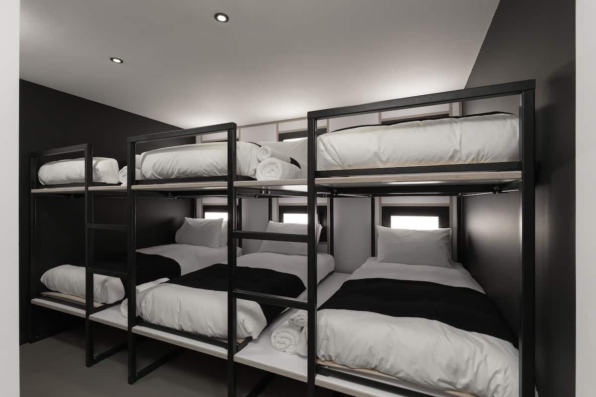 A bunk bed room with three levels, each with white bedding and black headboards.