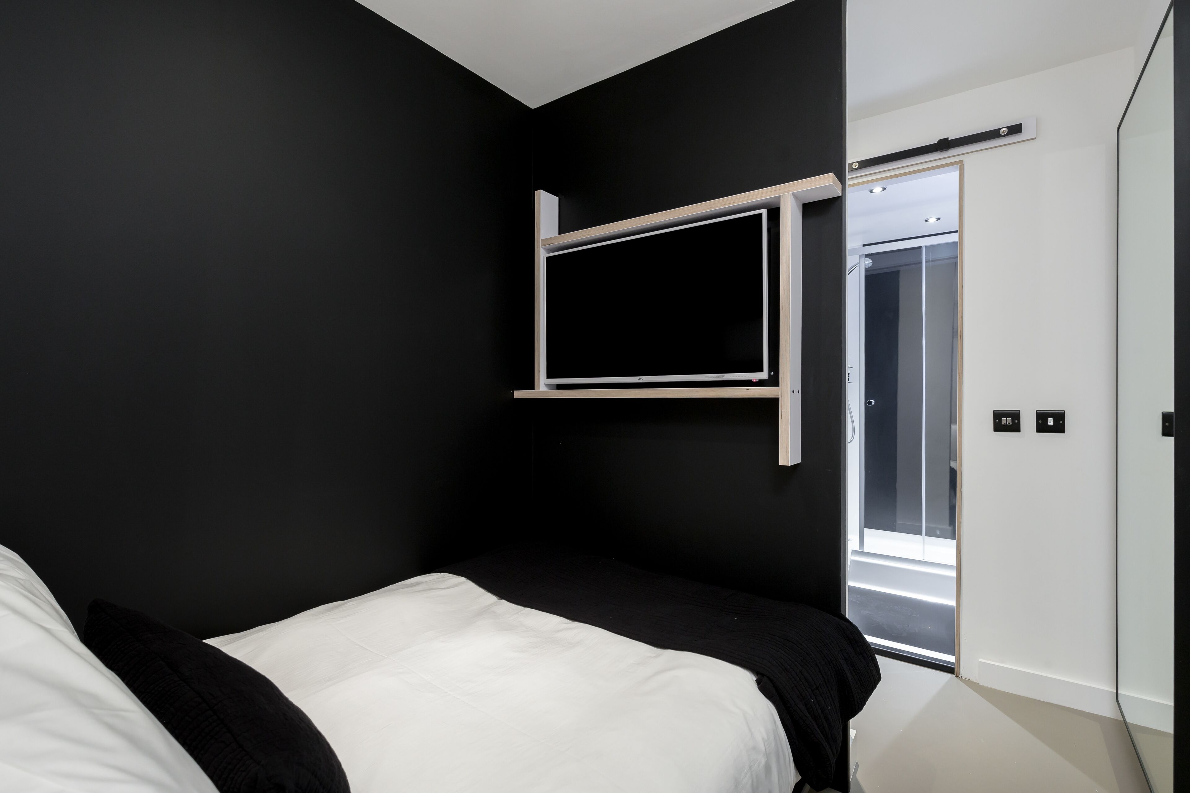 A modern bedroom with a bed, a mounted TV, and a sliding door leading to a bathroom.