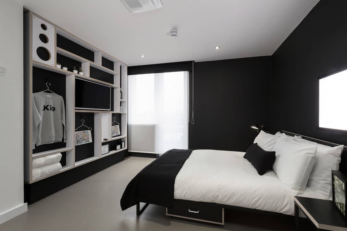 A modern bedroom with a bed, built-in wardrobe, and a large window.