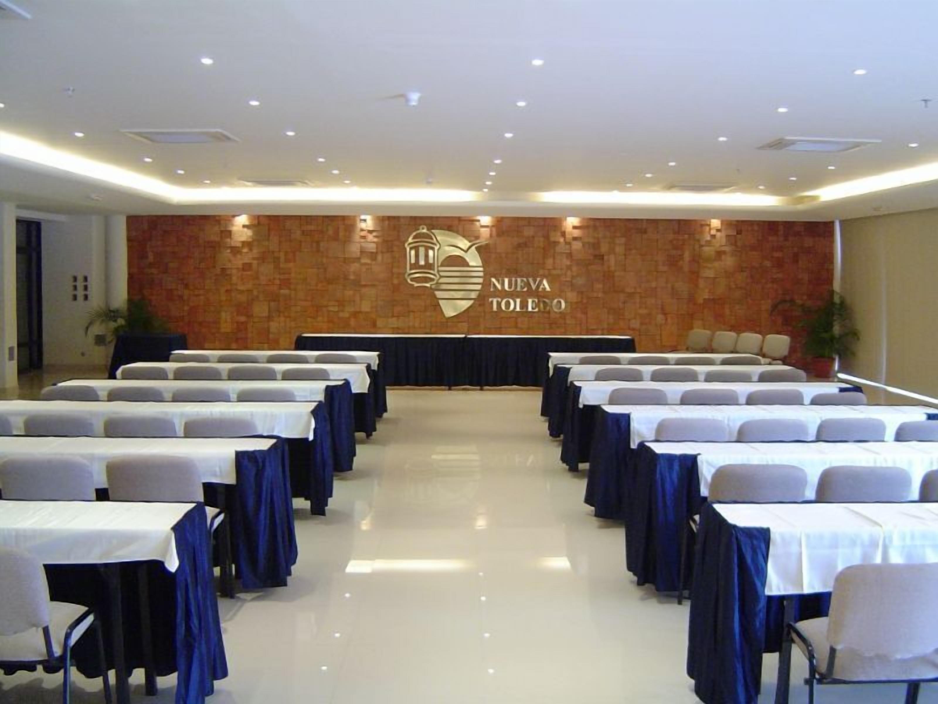 A conference room with rows of tables and chairs, a stone wall with a logo, and a polished floor.