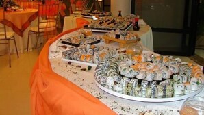 Een buffet met verschillende sushi gerechten, een sausfles en een glas water.