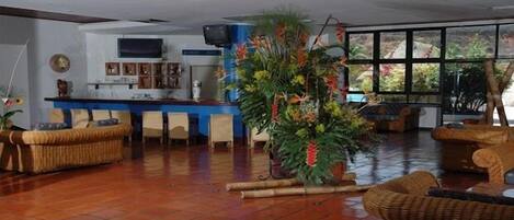 Un hall amplio con mostrador de recepción, mobiliario de mimbre y una gran planta de interior.