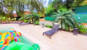 Un espace piscine équipé de chaises longues, d’un toboggan et agrémenté de diverses plantes.