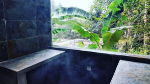 A room with a window overlooking a garden with large green leaves and plants. - La Semilla Ecolodge (24 de Diciembre)