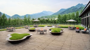 Un patio al aire libre con zonas de estar, vistas a las montañas y un edificio con grandes ventanales.