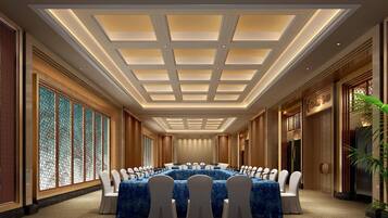 Un salón de conferencias con una larga mesa, sillas blancas e iluminación empotrada en el techo.