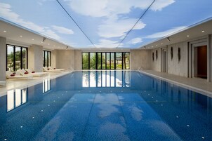 Una amplia piscina cubierta con paredes de vidrio transparente, un techo con diseño de cielo y vistas a zonas verdes exteriores.