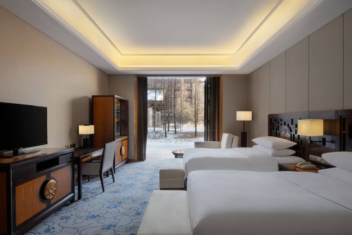 A hotel room with a large bed, a TV, a desk, and a view of a snowy outdoor area.