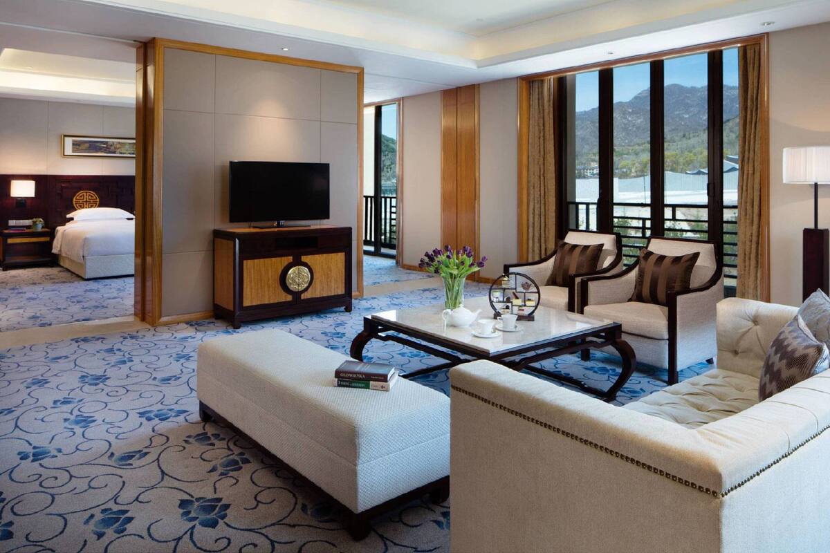 A hotel room with a large bed, a TV, a coffee table with a vase, and a view of a lake.