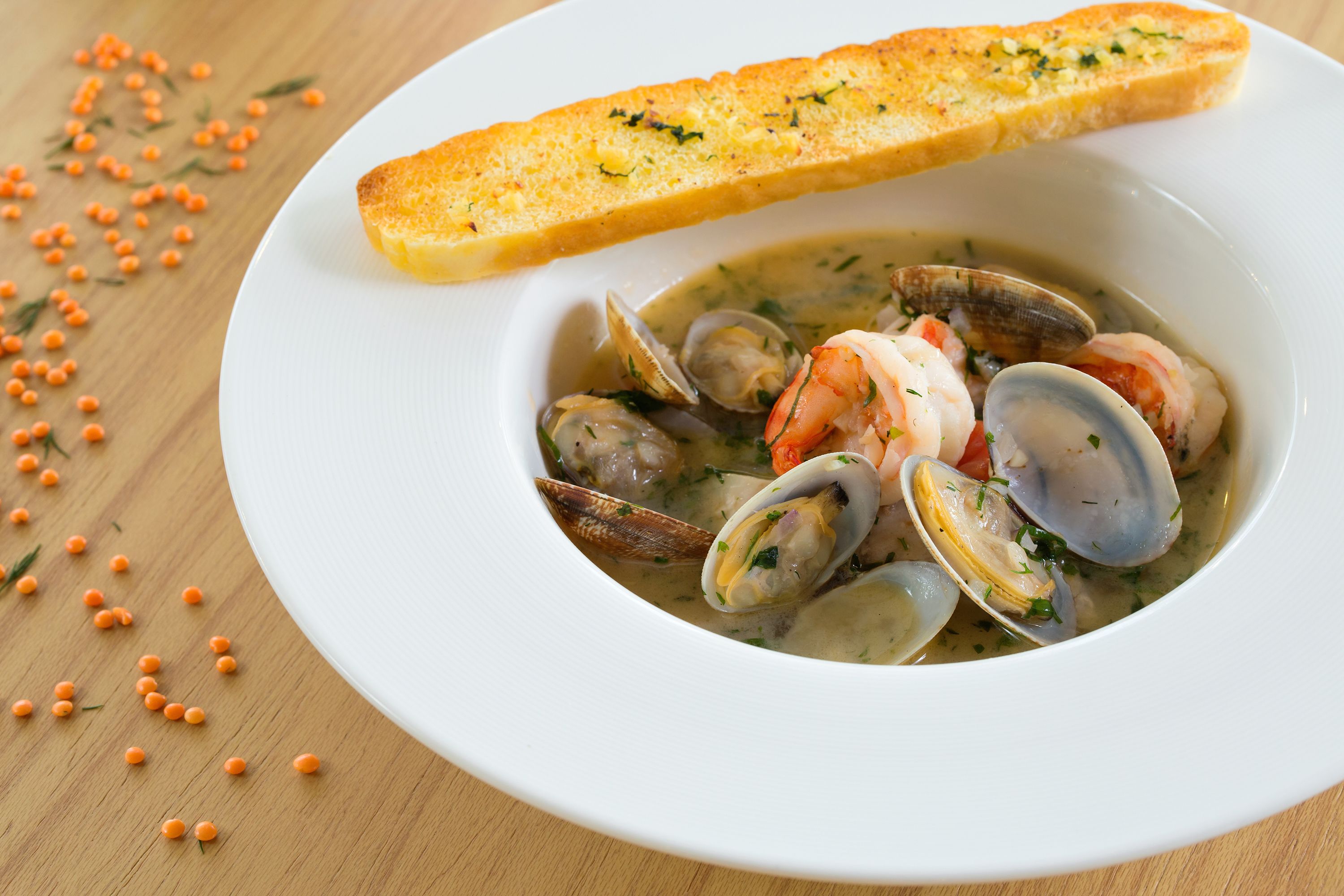 A bowl of seafood soup with clams and shrimp, accompanied by a slice of toasted bread.