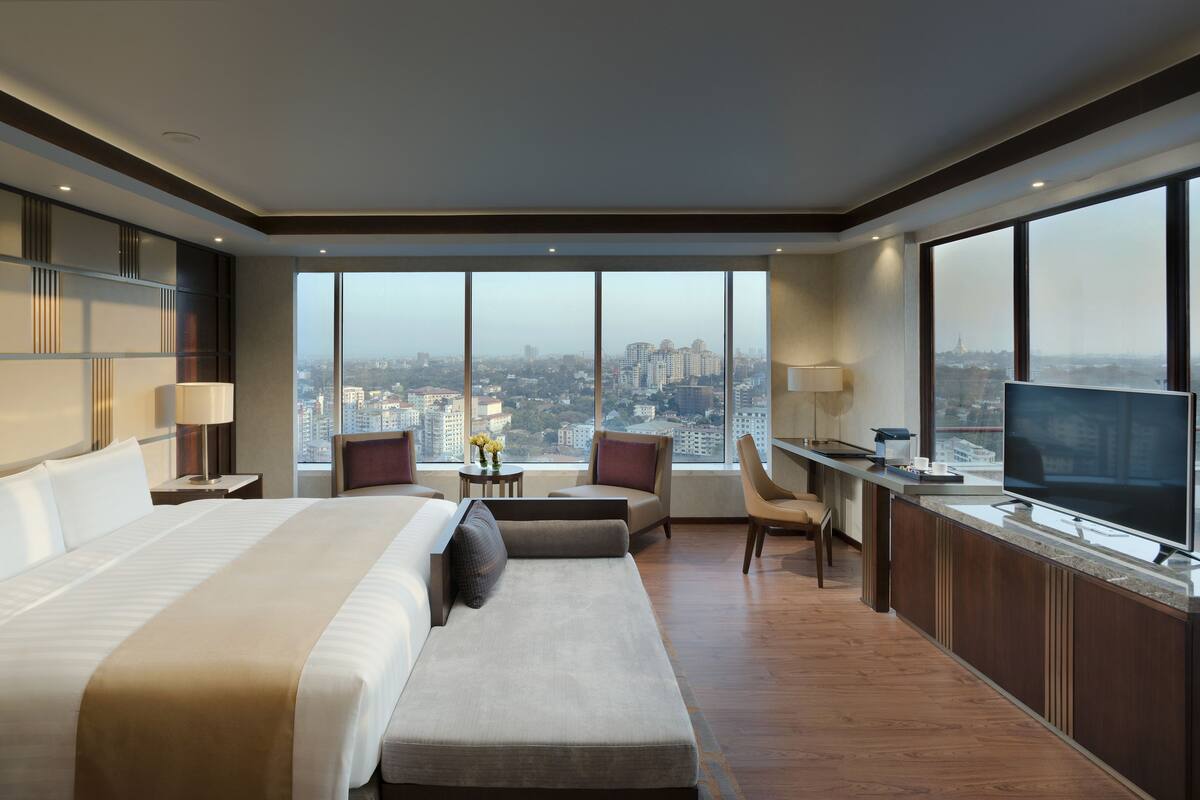 A modern hotel room with a large bed, a desk with a TV, and a view of the city.