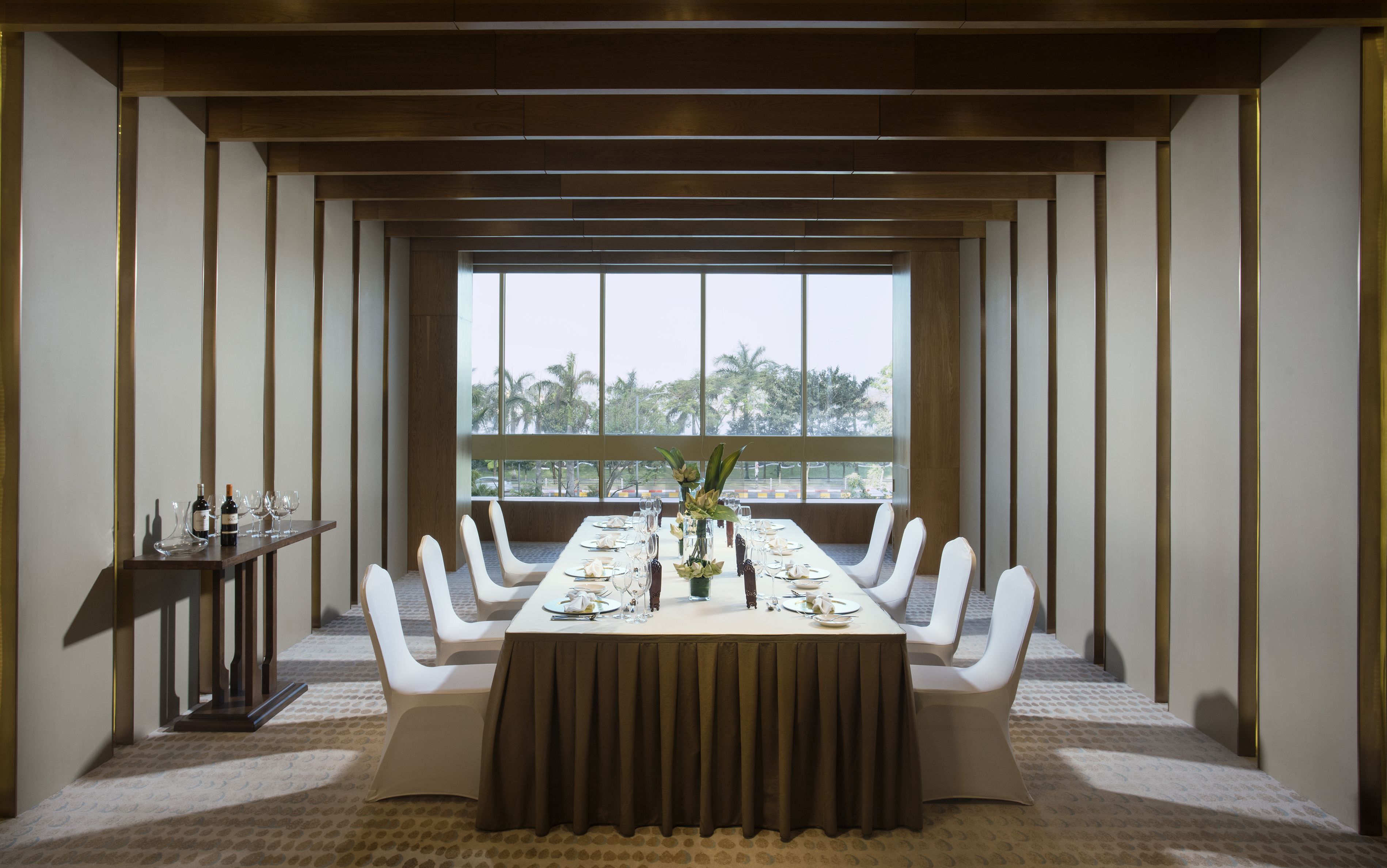 A conference room with a long table, white chairs, and a view of palm trees through large windows.