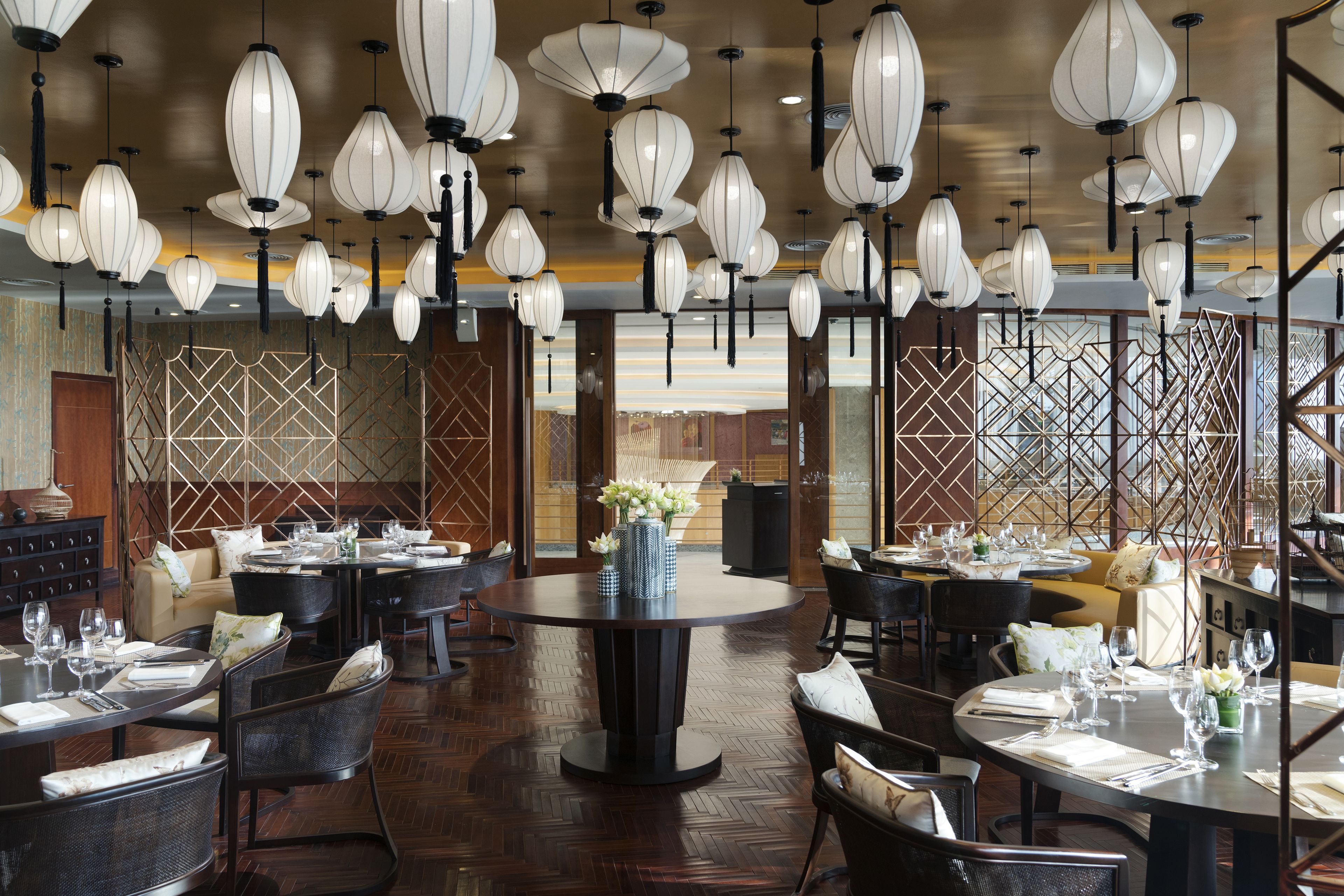 Een restaurant met ronde tafels, hangende lantaarnverlichting en een houten vloer.