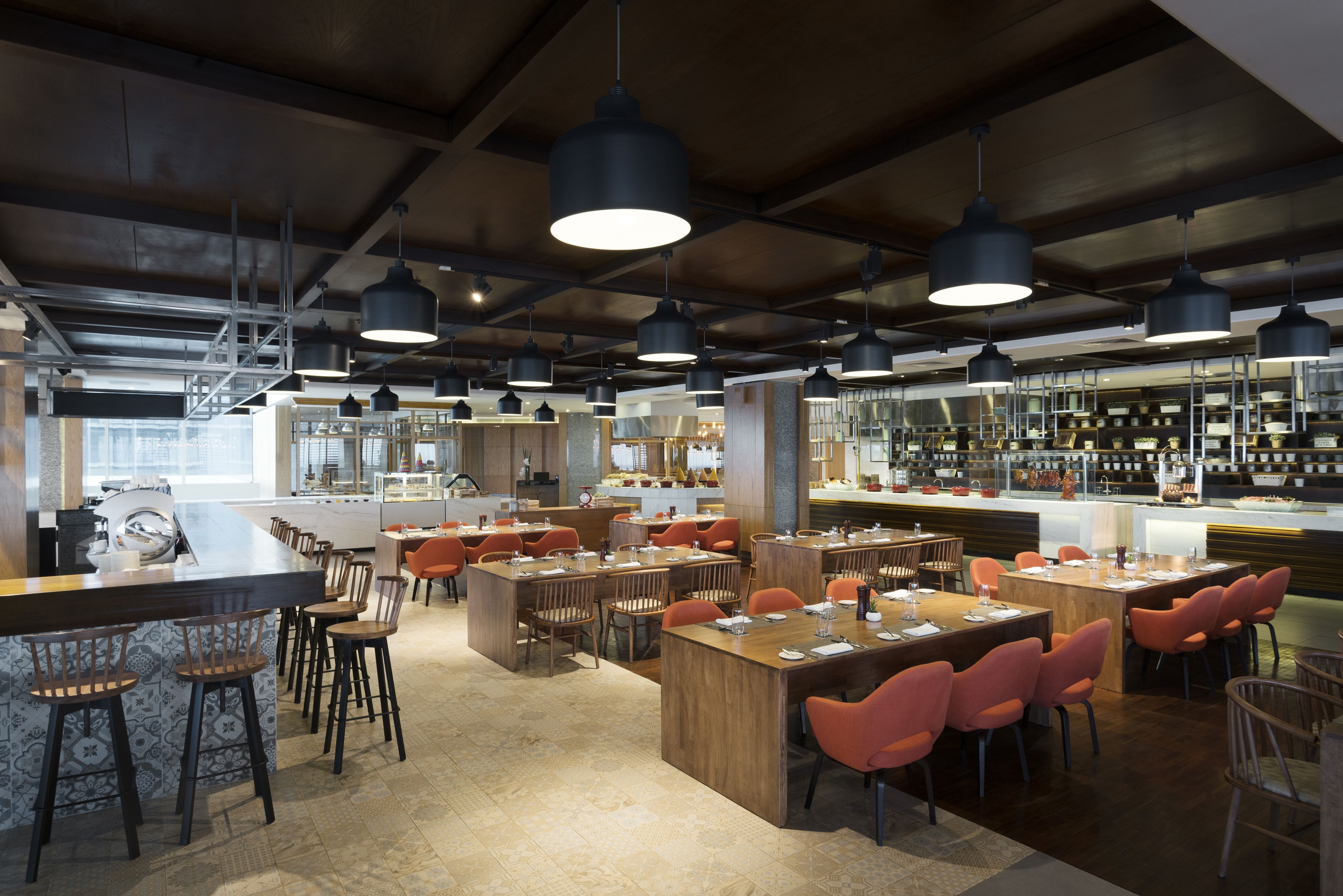 A modern restaurant with high ceilings, exposed beams, and pendant lighting. Tables are arranged in a spacious layout with bar stools and wooden chairs.