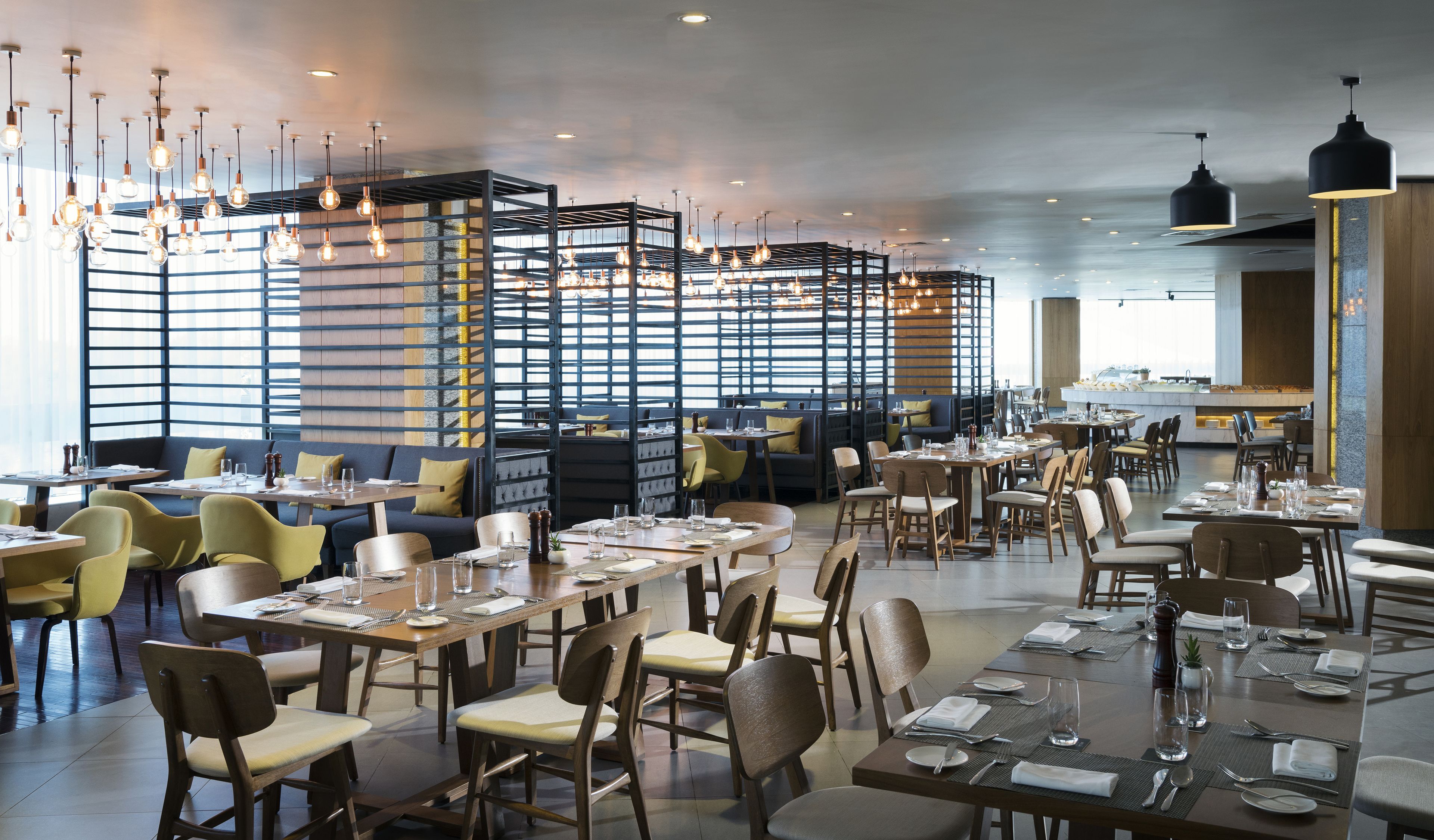 Interior de un restaurante moderno con techos altos, paredes de ladrillo visto y una variedad de opciones de asientos, incluyendo mesas y cabinas.