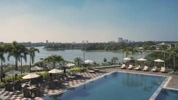 Relax by the serene pool, surrounded by lush greenery and a distant city view.