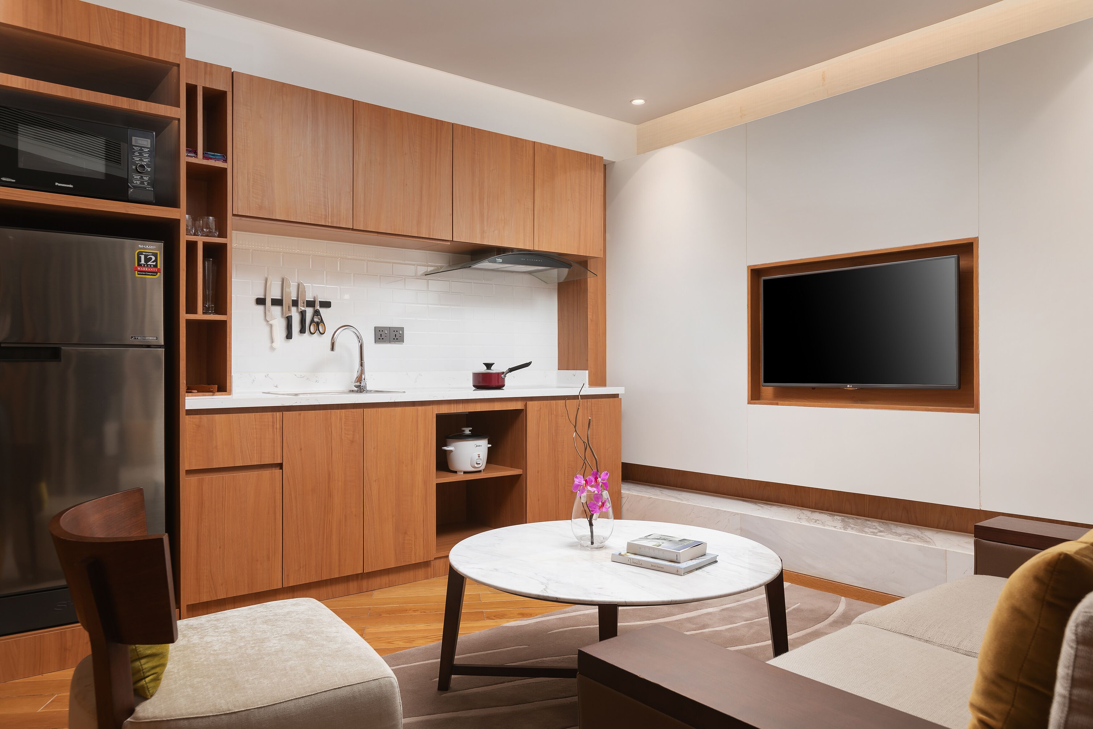 Una cocina moderna con armarios de madera, un microondas integrado y un televisor montado en la pared.