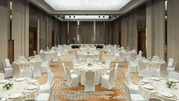 A banquet hall with round tables, white chairs, and a patterned carpet.