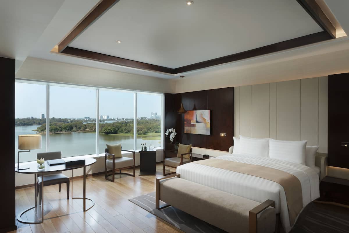 A modern hotel room with a large bed, a desk, and a view of a lake.