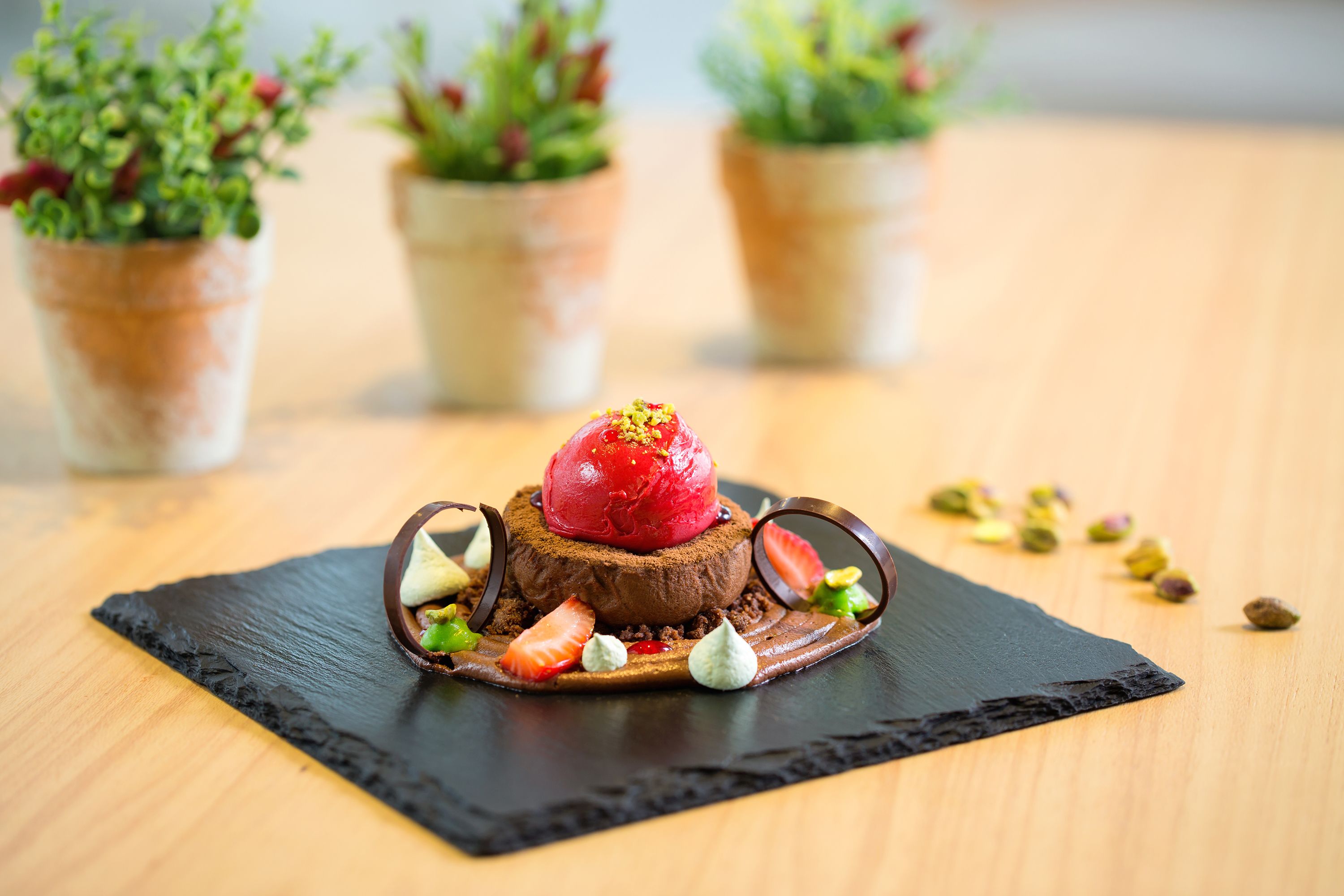 A dessert on a slate plate with chocolate base, strawberries, and a scoop of red ice cream.