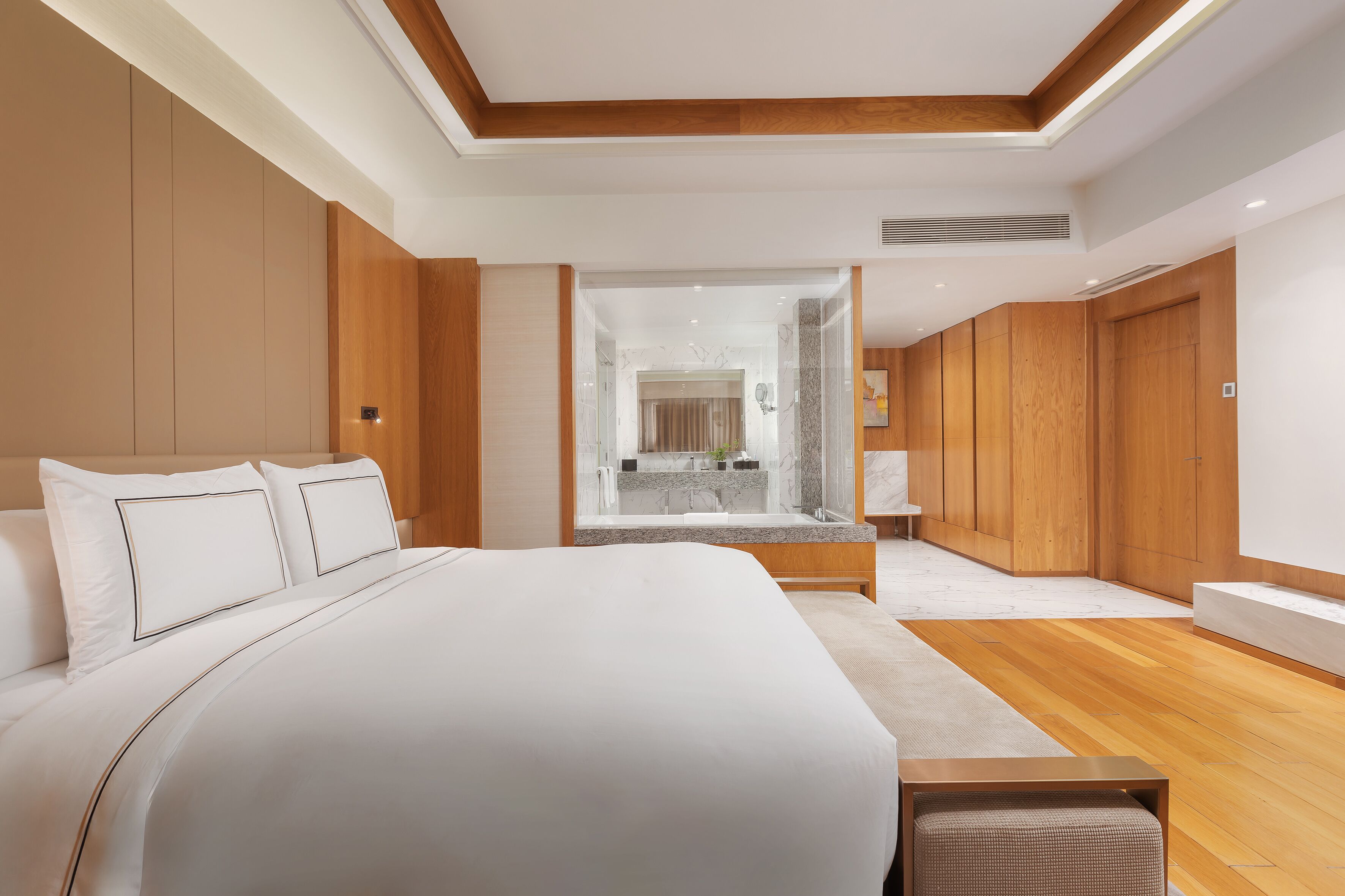Une chambre d’hôtel moderne dotée d’un grand lit, de lambris en bois, d’une salle de bain fermée par des parois de verre et d’un plancher en bois.