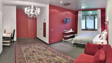 A modern hotel room with a red and white color scheme, a large bed, a TV, a chandelier, and a view of the outdoors.