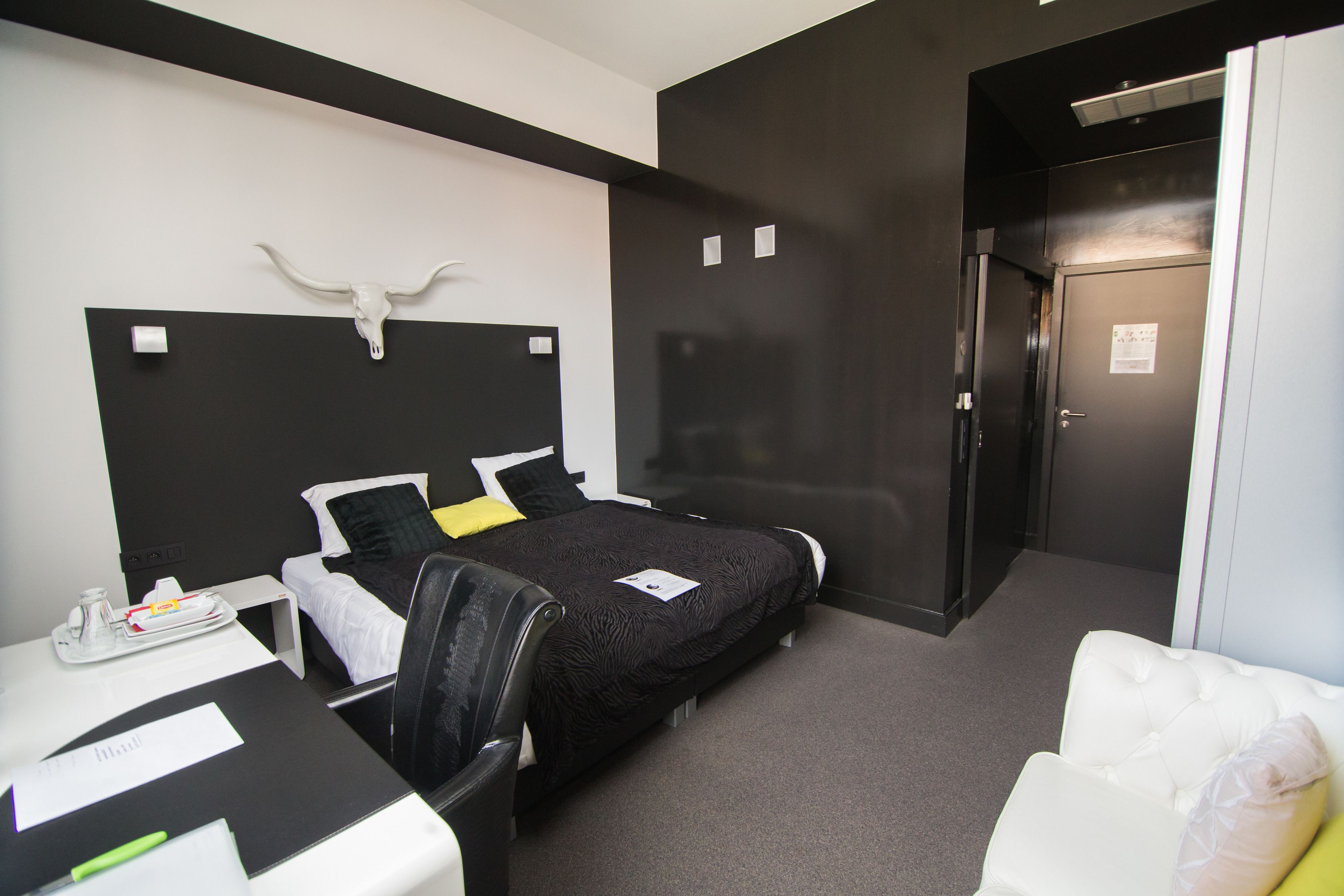 A hotel room with a bed, a desk with a tray of breakfast items, a chair, and a white couch.
