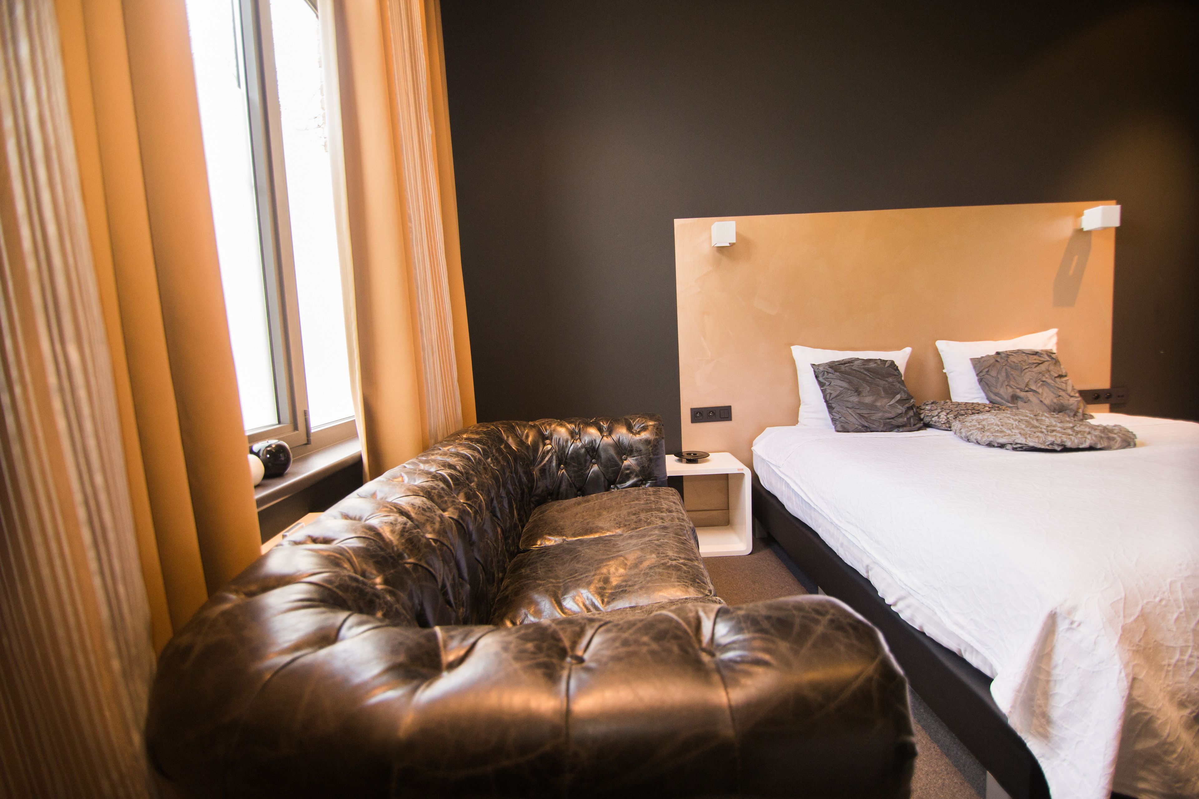 A modern bedroom with a large bed, a leather sofa, and a nightstand.