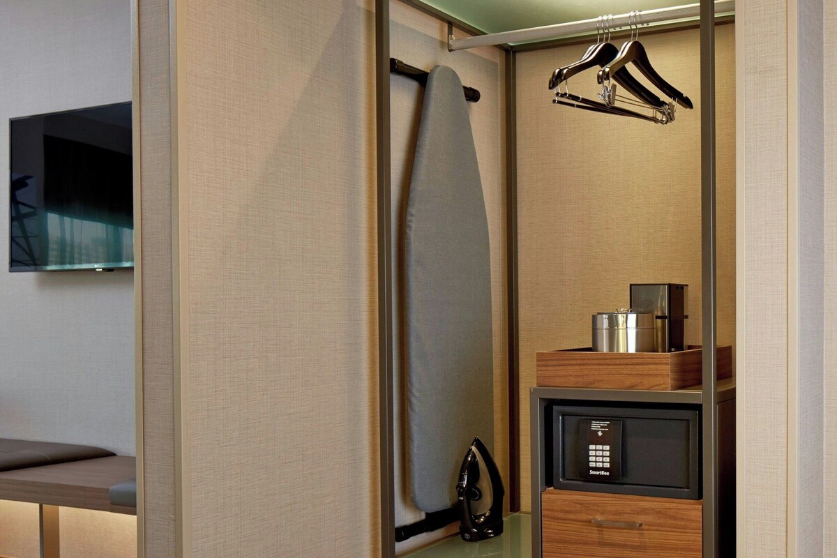 Un closet pequeño con espacio para entrar, una barra para colgar ropa, un estante con una tetera y un microondas.