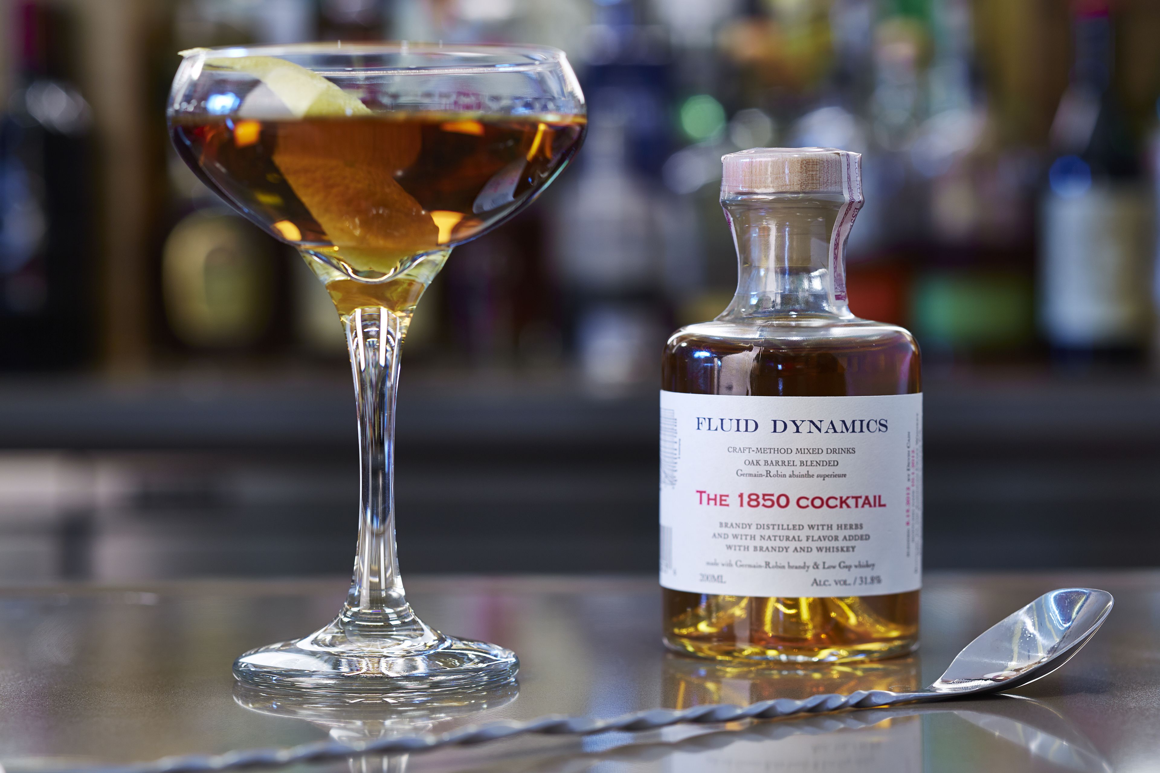 A cocktail glass and a bottle of 'The 1850 Cocktail' on a bar counter.