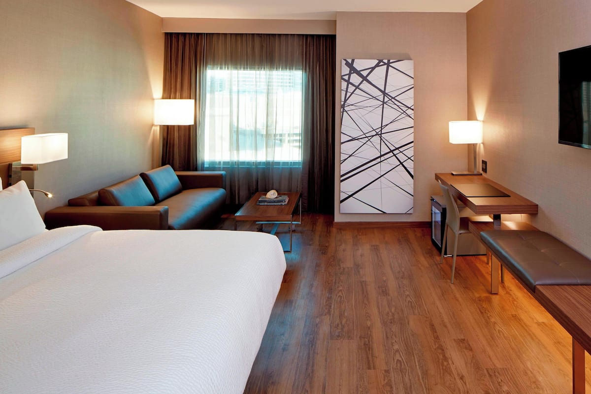 A hotel room with a large bed, a sofa, a desk, and a TV.