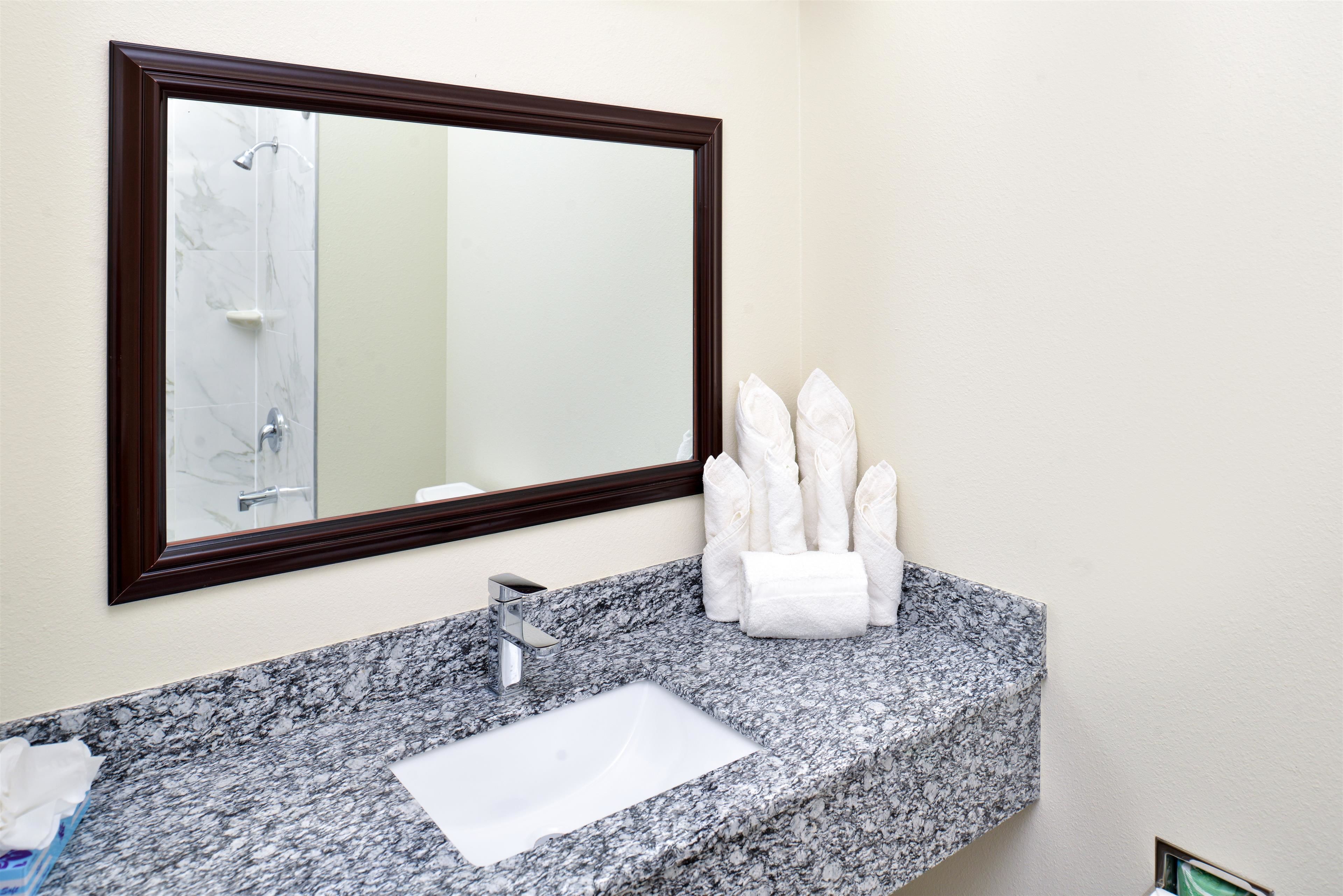 A bathroom with a marble sink, a large mirror, and a towel rack with folded towels.