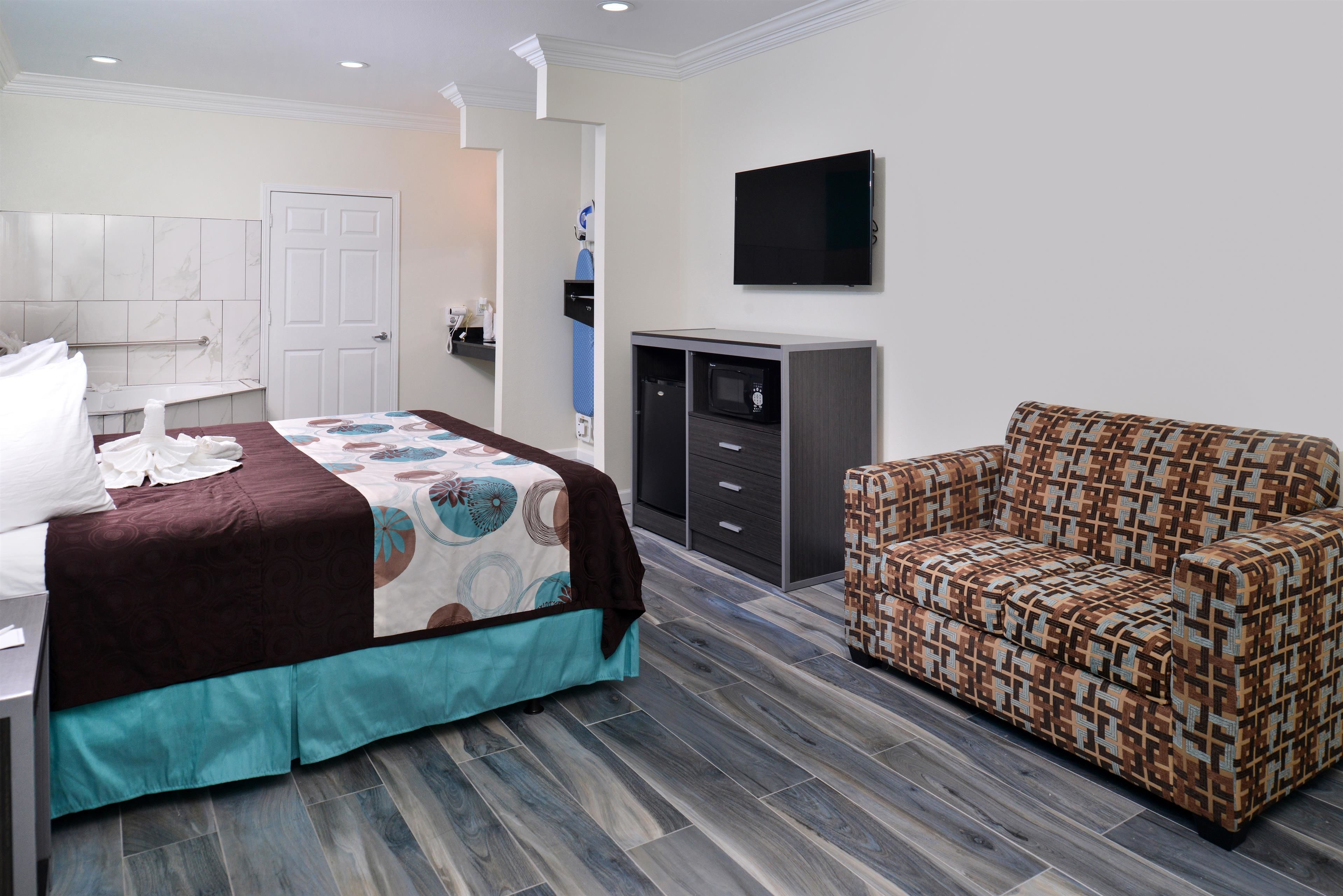 A hotel room with a bed, a sofa, a TV, a minibar, and a bathroom.
