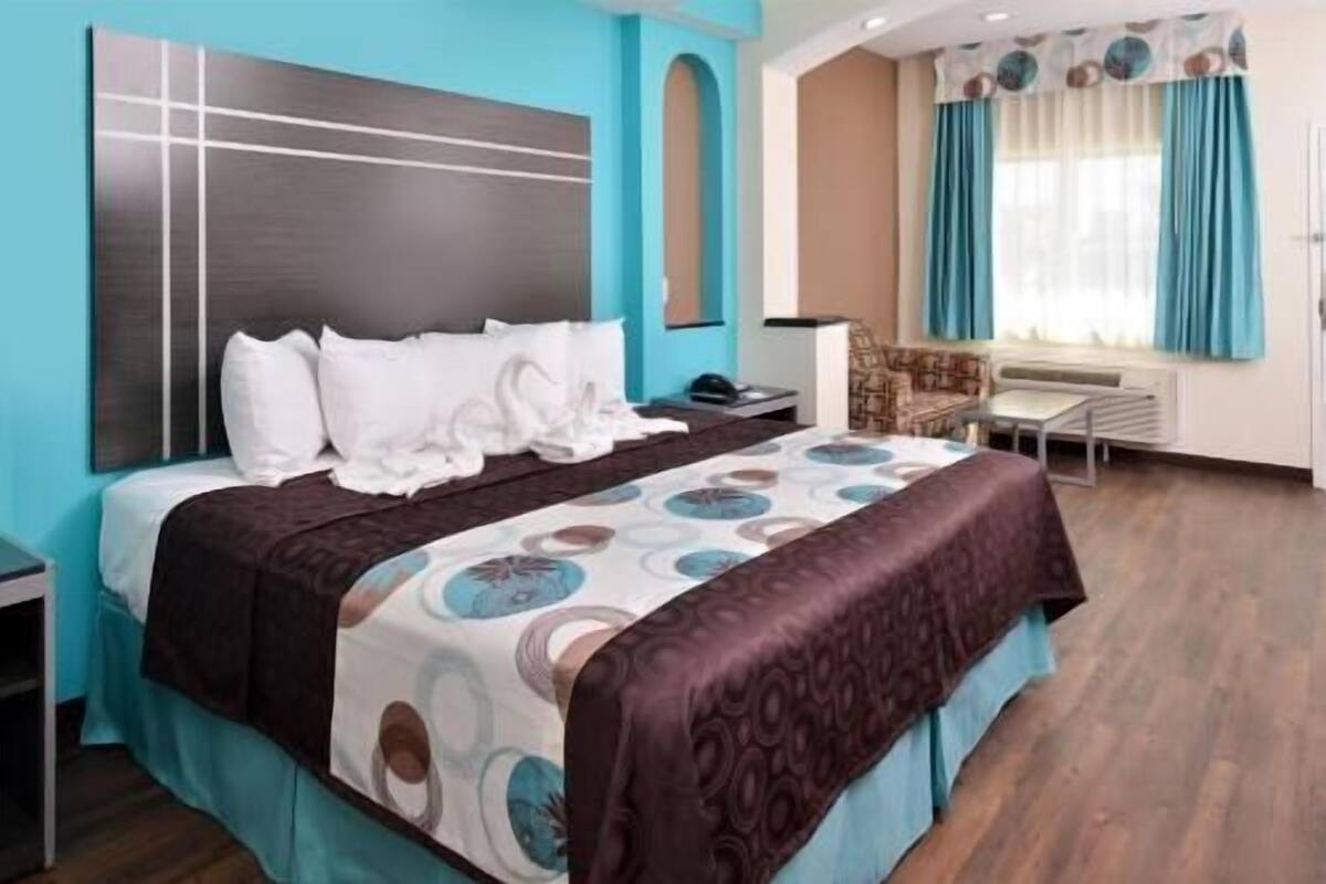 Une chambre d’hôtel avec un lit, une table de chevet, une chaise et une fenêtre avec des rideaux.