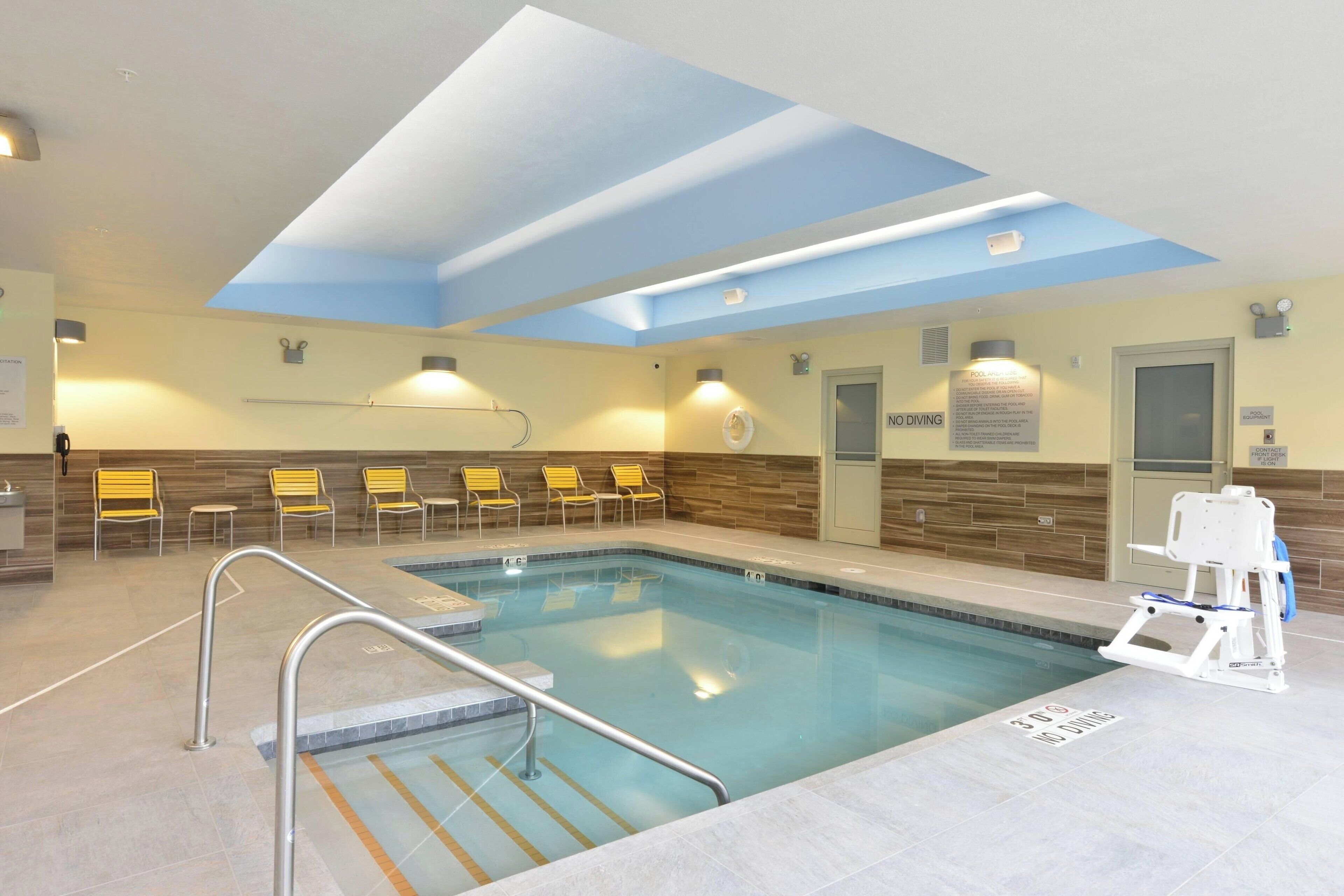 An indoor swimming pool with a ceiling skylight, yellow chairs, and a lifeguard stand.