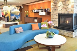 Um lobby moderno com um sofá azul, uma mesa de centro redonda, lareira e um balcão de recepção.