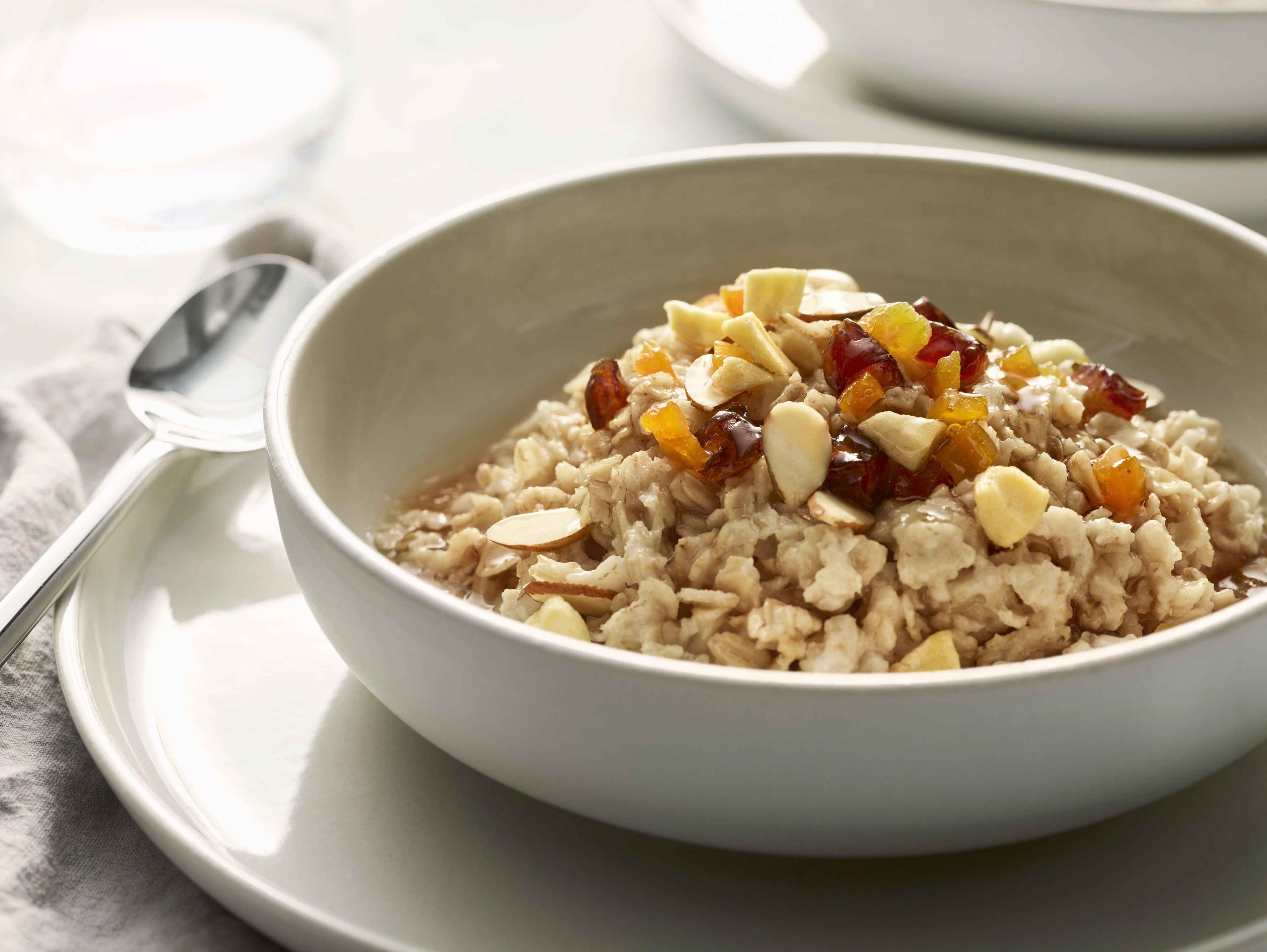 A bowl of oatmeal with nuts and dried fruit on a white plate.