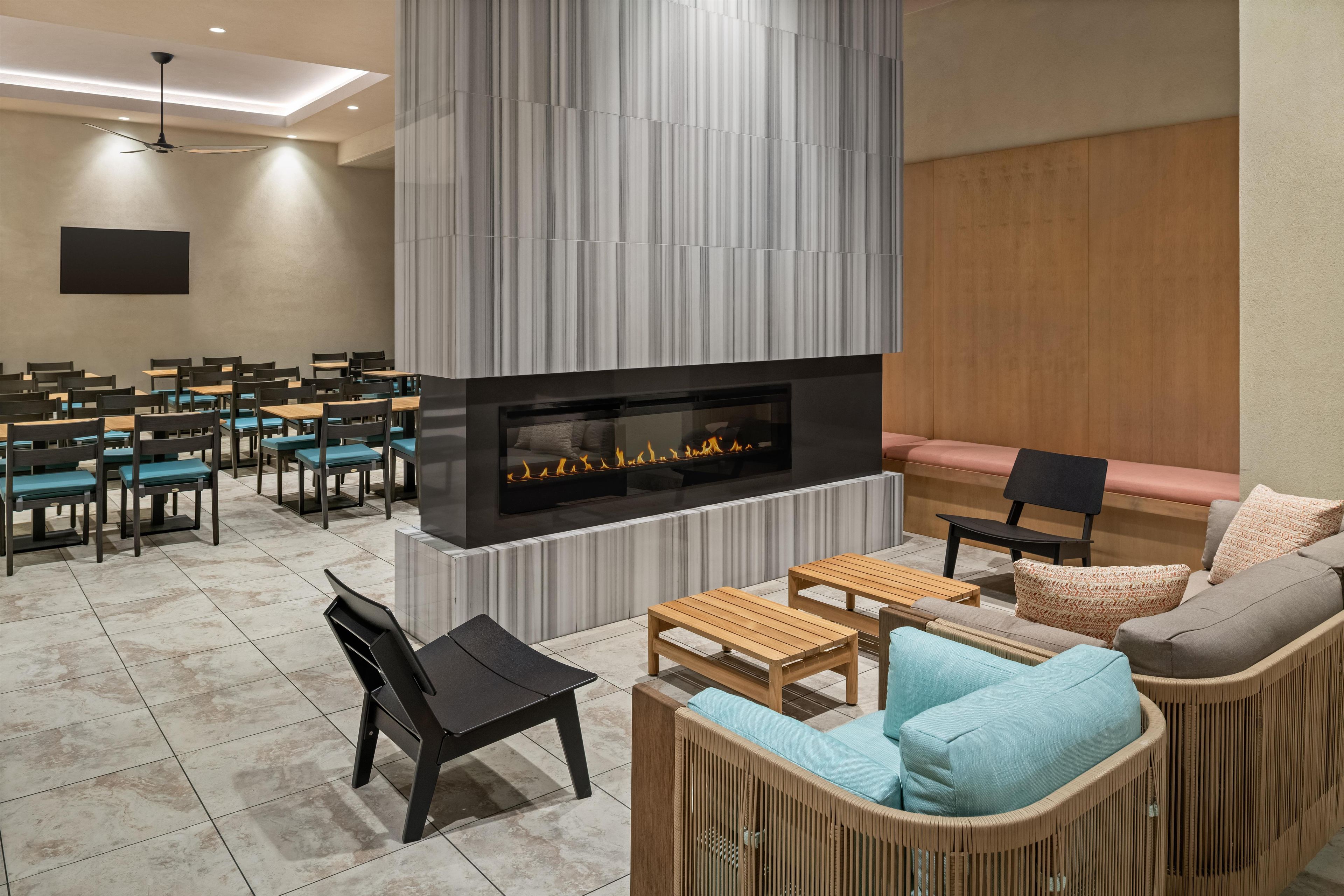 A modern lounge area with a fireplace, seating arrangements, and a ceiling fan.