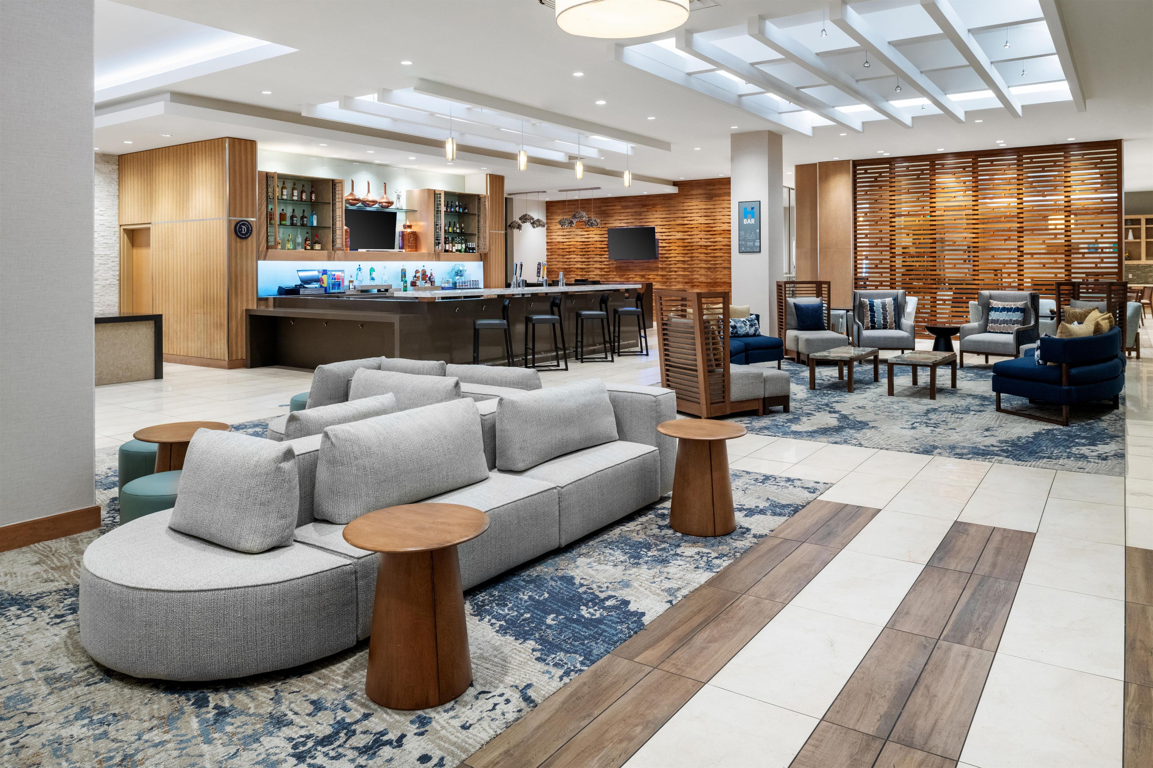 A modern hotel lobby with a bar area, seating, and a large screen.