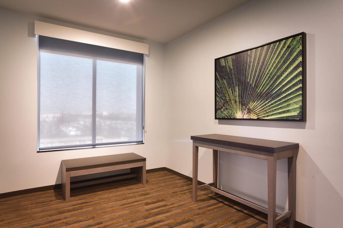 A room with a large window, a bench, and a table against a white wall.