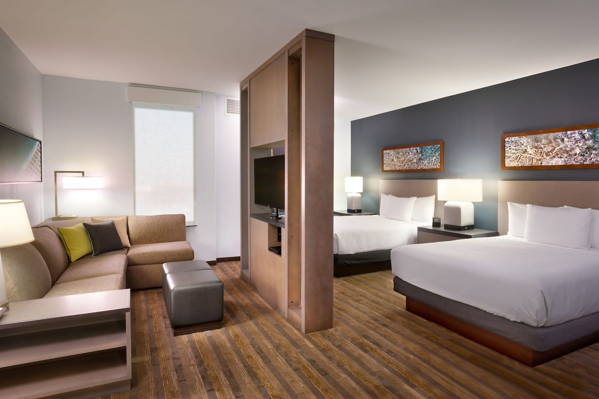 A hotel room with a sofa, two beds, a TV, and artwork on the walls.