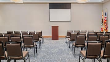 Ein Konferenzraum mit Reihen von Stühlen, die zu einem Rednerpult, Flaggen und einer Projektionsleinwand zeigen.