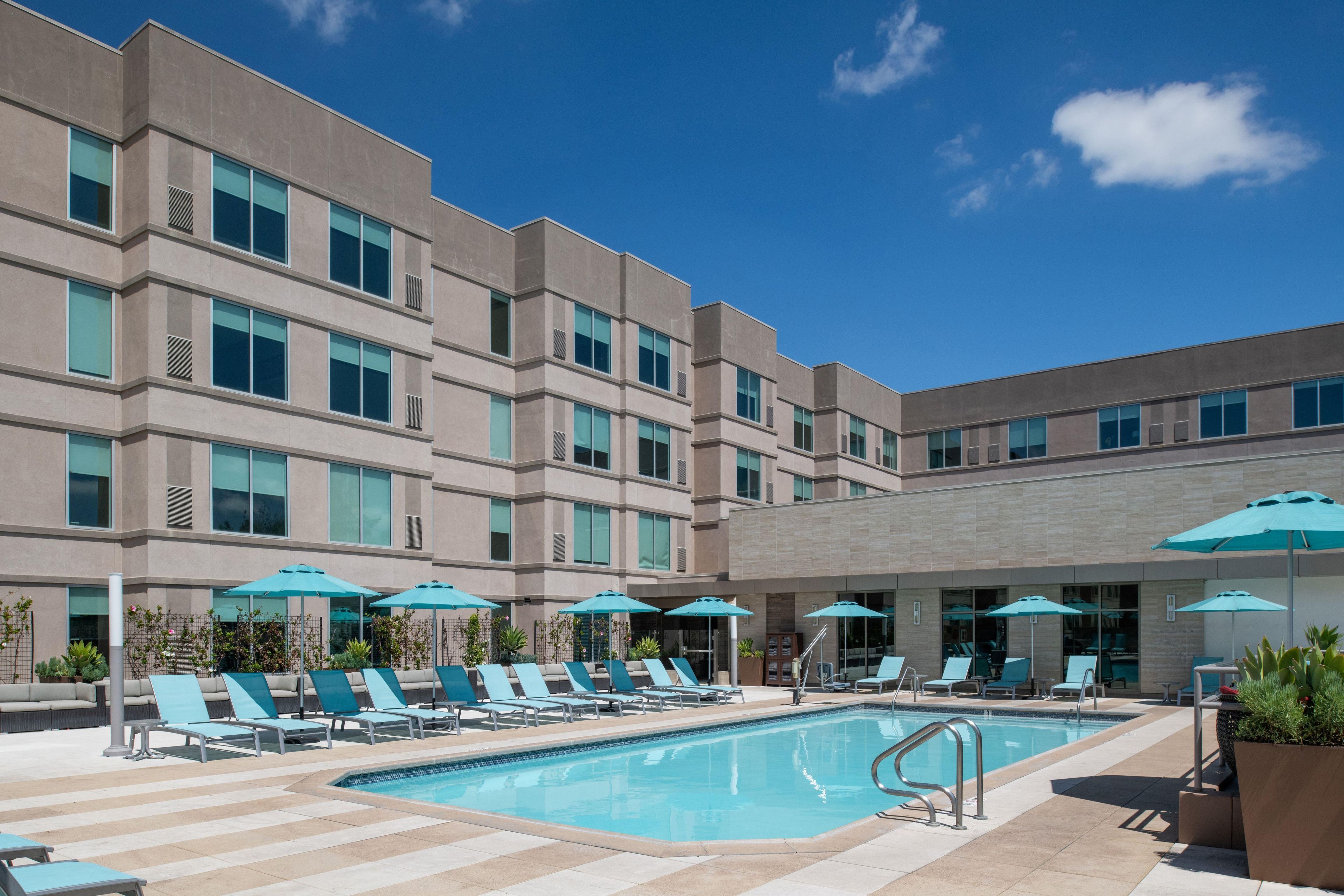 Ein modernes Hotel mit Schwimmbad, Liegestühlen und Sonnenschirmen.