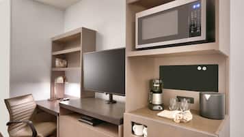 A modern hotel room with a flat-screen TV, a coffee maker, a microwave, and a small cabinet.